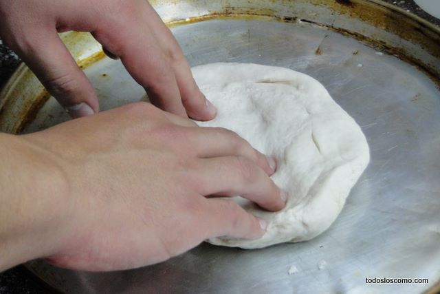 Manos extendiendo un bollo de masa de pizza en una pizzera